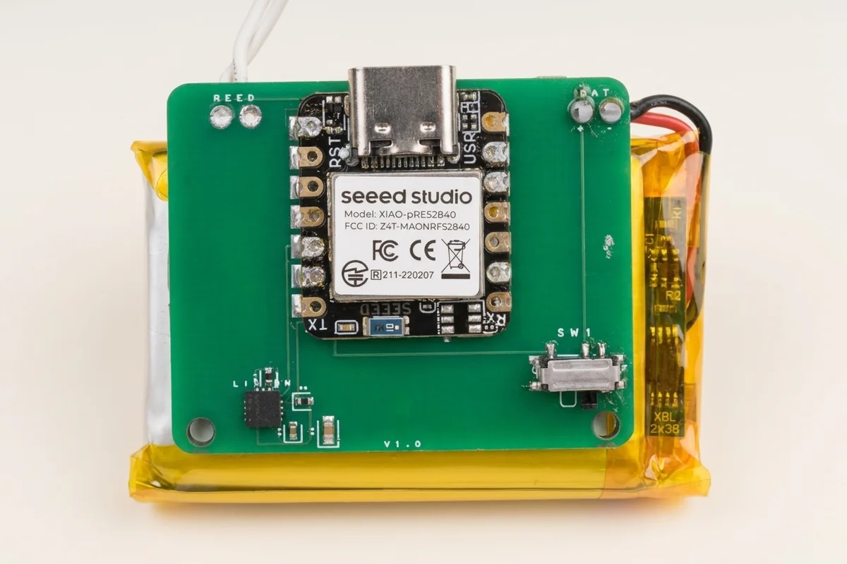 A green circuit board with a XIAO nRF52840 sitting on a yellow battery pouch